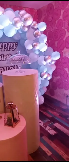 A birthday setup with a balloon pillar, a Happy Birthday sign and a lit backdrop