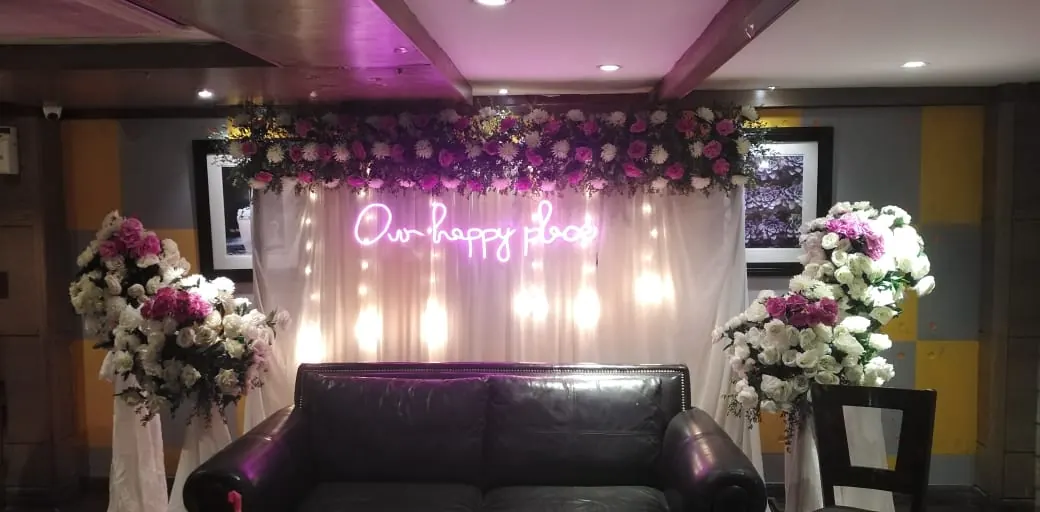 A wedding stage with a soft floral backdrop and an Our Happy Day sign